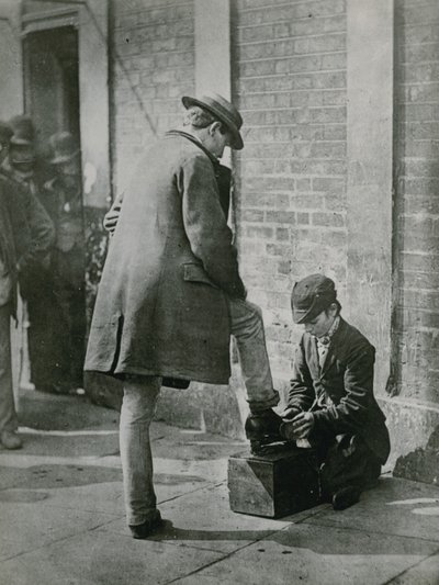 Een jonge schoenpoetser die de schoenen van een man op straat poetst door English Photographer